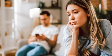woman looking sad while man plays on phone