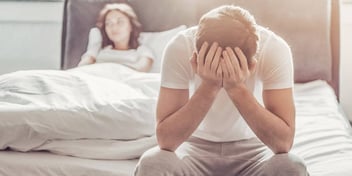 woman in bed upset at man sitting at foot of bed 