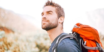 man with backpack looking at mountains