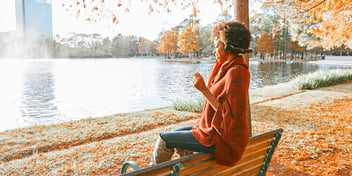 woman seated on bench by lake autumn leaves