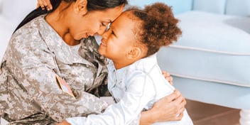 mom in military uniform hugs young daughter