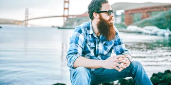 bearded man sits on rock by golden gate bridge and the bay