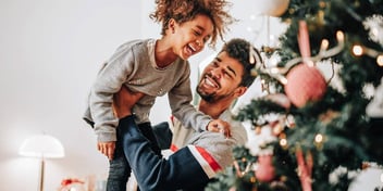 dad lifts daughter up in his arms to see holiday tree