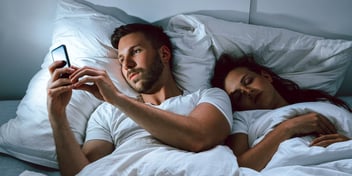couple in bed man looking at phone