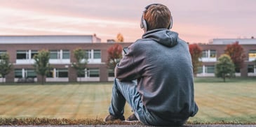 kid sitting outside school wearing hoodie and headphones 