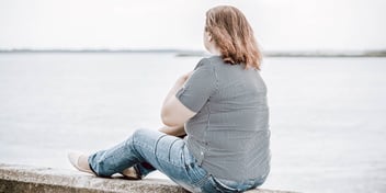 woman sitting on seawall looking out at water