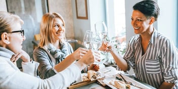 three female friends clinking wine glasses at table