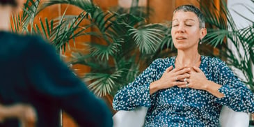 woman sits in chair with eyes closed talking to therapist