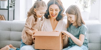 mom and two young girls smiling and unpacking a box