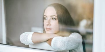 woman resting chin looking wistfully out window 