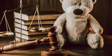 large teddy bear on desk next to judge gavel and stack of books