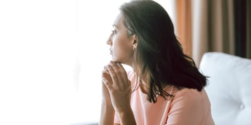 woman looks out sunny window while deep in thought