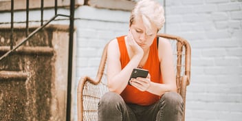 woman with chin in hands looks at phone with frustration