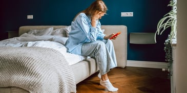 woman sitting on edge of bed with phone