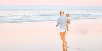 mom walks on beach while holding toddler