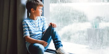 young boy sitting in a window looking outside