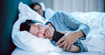 couple in bed man looks at phone woman looks jealous