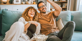 couple laughing sharing popcorn on couch