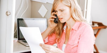 woman on the phone holding paperwork and looking confused