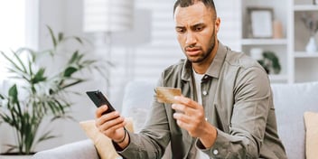 confused looking man holding a credit card and phone