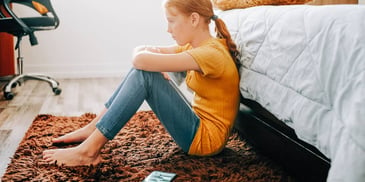 sad adolescent girl sitting on her bedroom floor