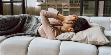 depressed woman laying on a couch with her hands over her eyes