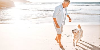 older man walking on the beach with a golden retriever