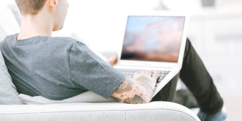 man with tattooed arms typing on a laptop