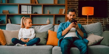 daughter glaring at her dad sitting next to her and ignoring her while on his phone