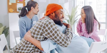 Black man hugs white woman at a group therapy session