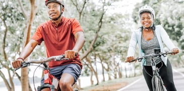 man and woman smiling and riding bikes through a park