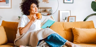 smiling woman relaxing on a couch with a book and cup of tea