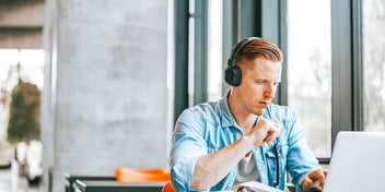 redheaded man wearing headphones and working in a cafe