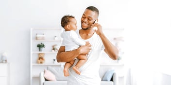 black father holding infant daughter and talking on his phone