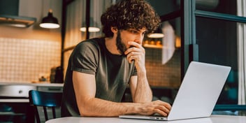 man with a mop of curly brown hair staring intently at a laptop