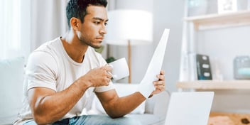 man drinking coffee while reading a piece of paper