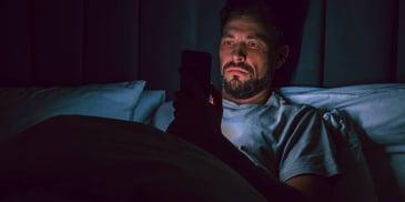 man playing games on his phone in the dark while in bed