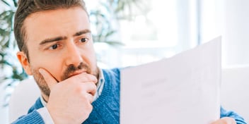 man holding his chin and reading a piece of paper