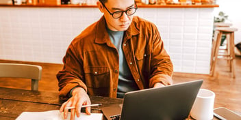 man working on his laptop and taking notes