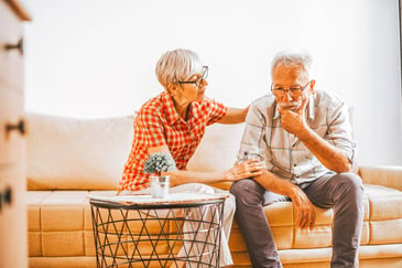 retired couple sitting on couch woman with her hand on his shoulder