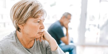 Older woman looking distraught with older male partner in the background also distraught.