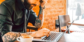man with tattooed arms working on his computer in a cafe