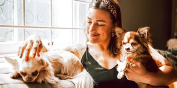 woman petting her two tiny dogs on a couch and smiling