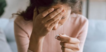 grieving woman holding an engagement ring and holding her head