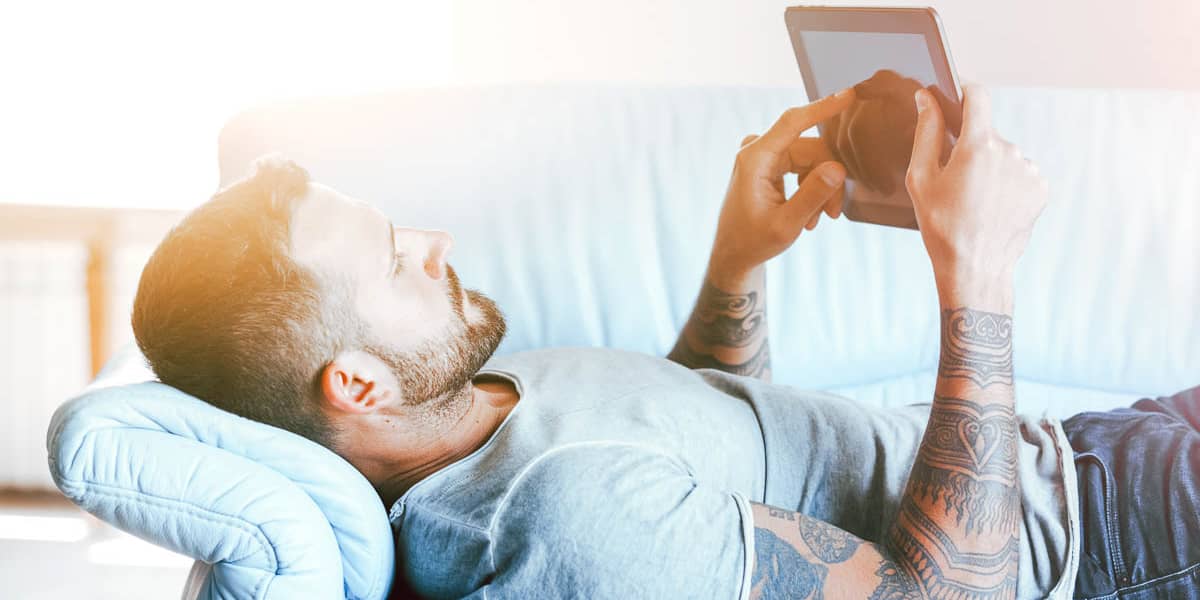 Young male laying on couch using tablet